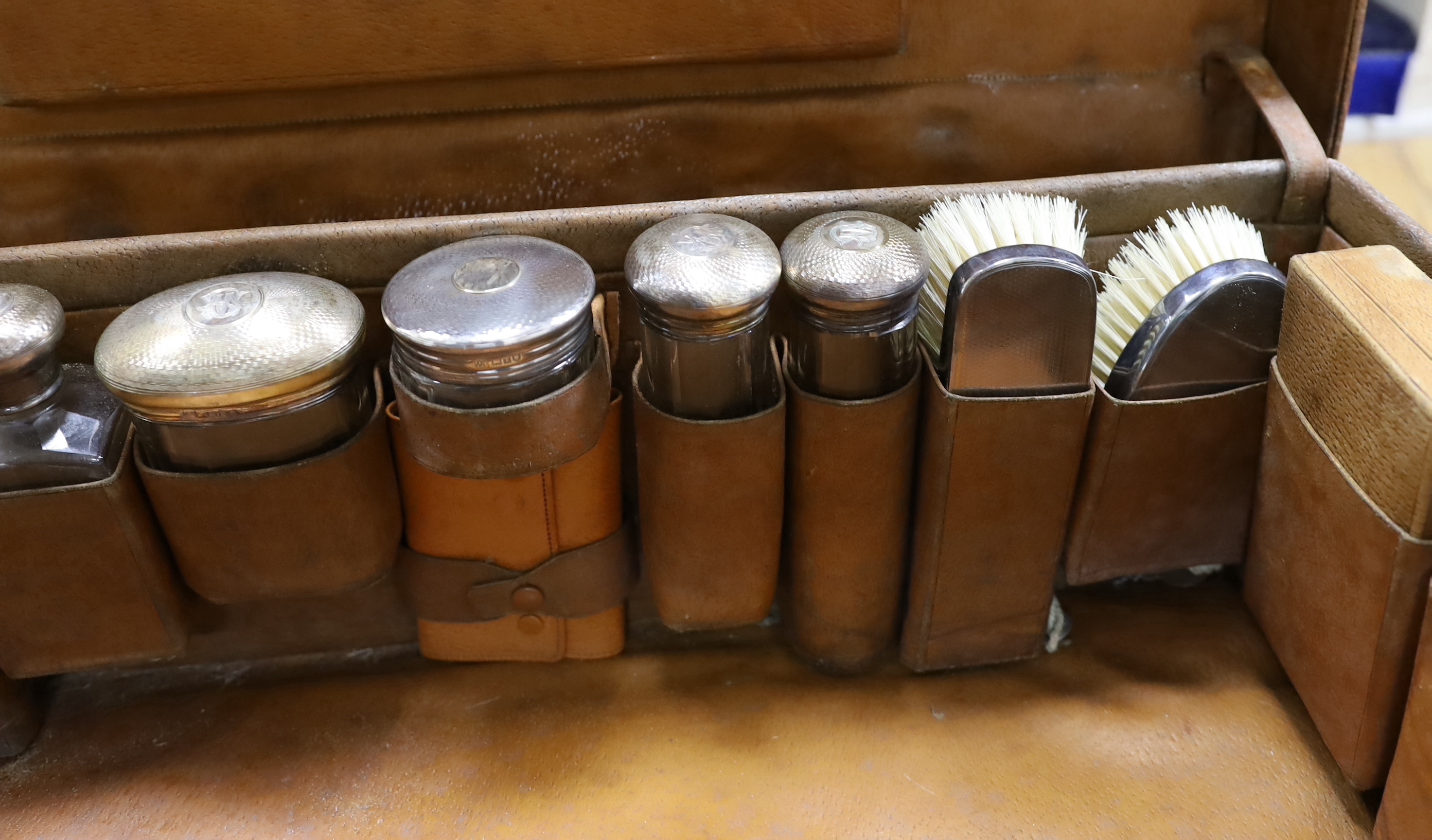 An Edwardian leather travelling toilet case, containing eleven silver mounted toilet jars etc. including a mounted glass hip flask and easel mirror, Drew & Sons, London, 1905, case width 62.5cm.